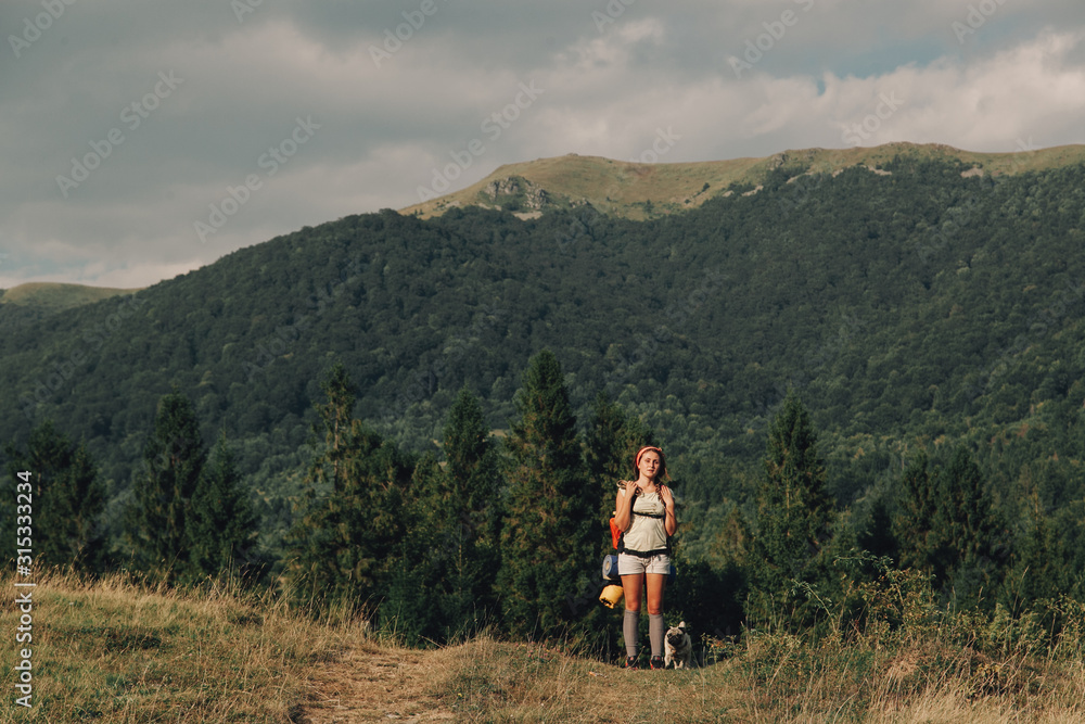 Photo of a beautiful young woman with pug on the hill among the mountains early in the morning.