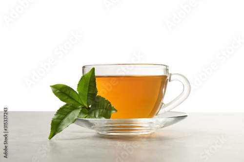Cup of green tea and leaves on grey table