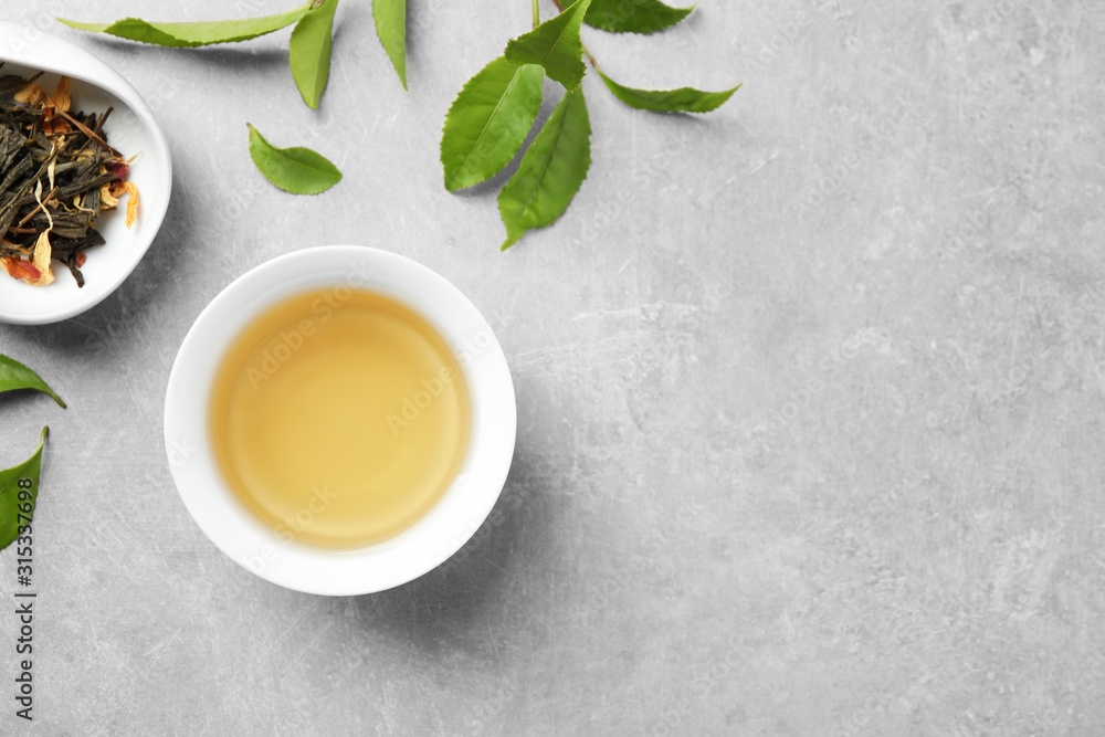 Cup of green tea, dry and fresh leaves on grey table, flat lay. Space for text Cup of green tea, dry and fresh leaves on grey table, flat lay. Space for text