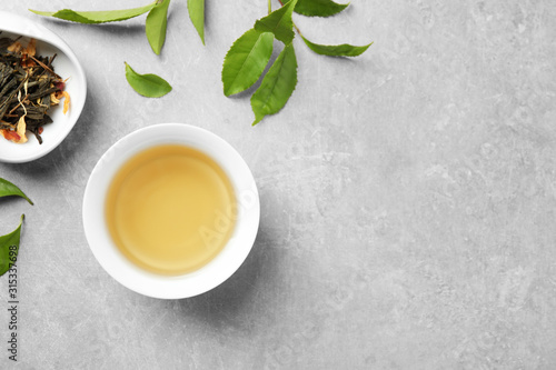 Cup of green tea, dry and fresh leaves on grey table, flat lay. Space for text