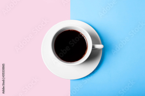 white cup of coffee on pink and blue pastel background top view
