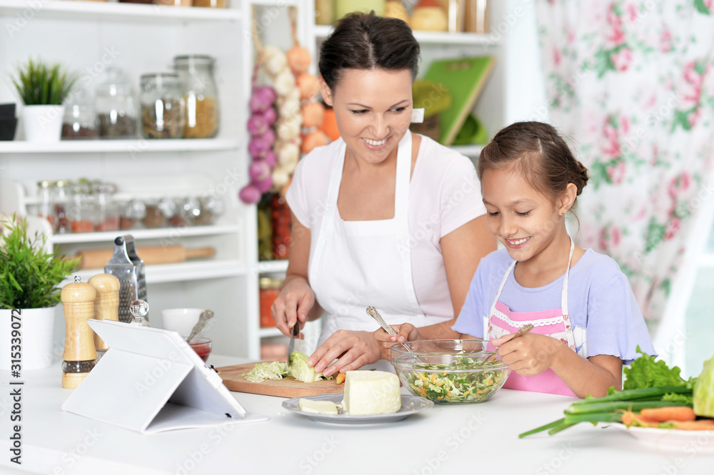 Cute little girl with her mother cooking together at kitchen table