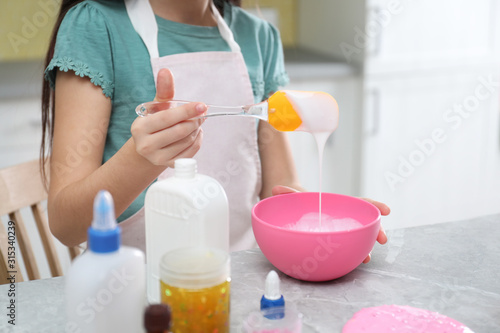 Little girl mixing ingredients with silicone spatula at table in kitchen  closeup. DIY slime toy