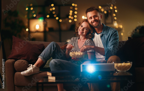 Family couple watching television projector at home on sofa.
