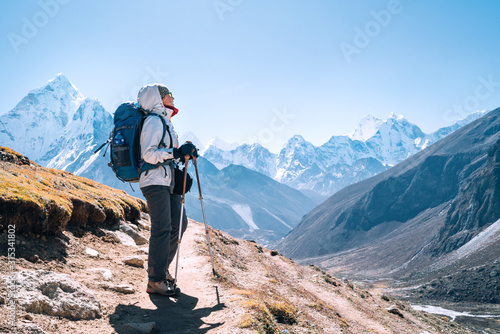 Young hiker backpacker female taking a walking with trekking poles during high altitude Everest Base Camp route near Dingboche,Nepal. Ama Dablam 6812m on background. Active vacations concept photo