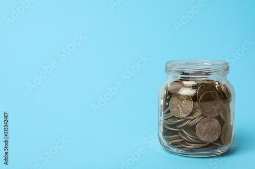 Glass jar with coins on light blue background, space for text