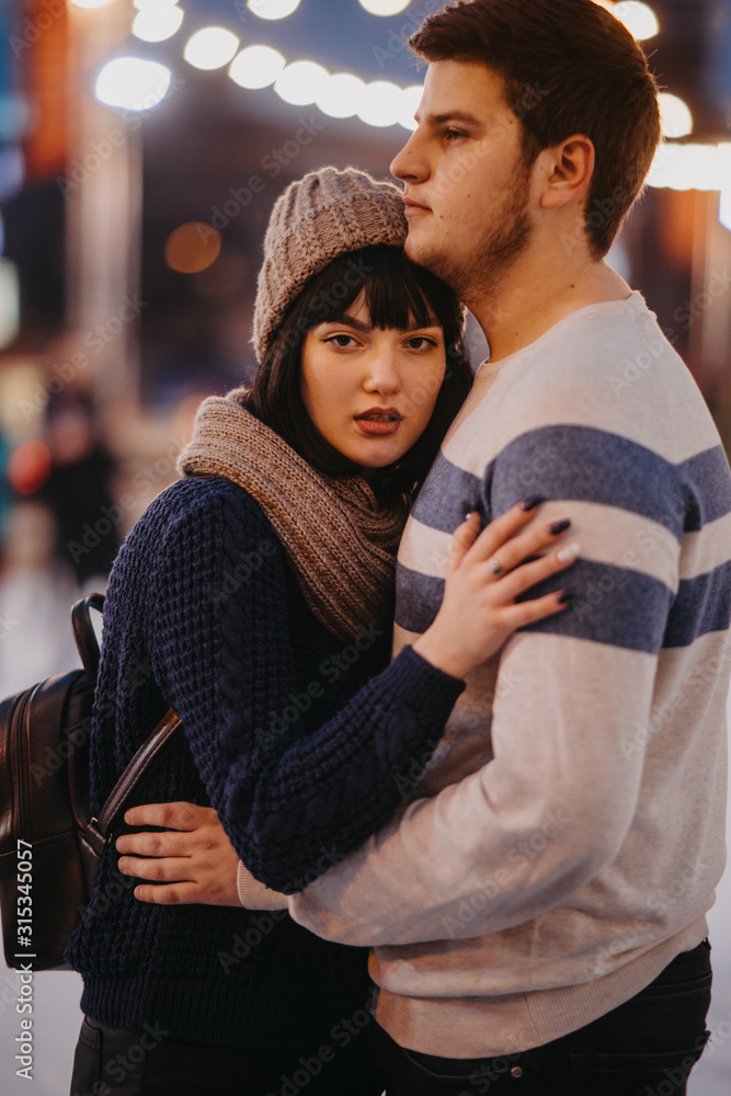 Fototapeta premium Young couple stands and embraces on the background city lights.