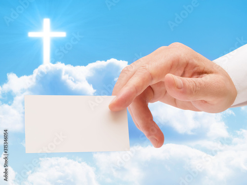 Religious man hand presenting blank white card against cloudy sky with illuminated cross photo