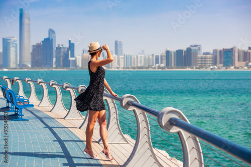 Obraz na płótnie Tourist woman enjoying view of Abu Dhabi with sea and skyscrapers. Sunny summer day in Abu Dhabi - famous tourist destination in UAE. Ideal place for luxury travel and rest w salonie