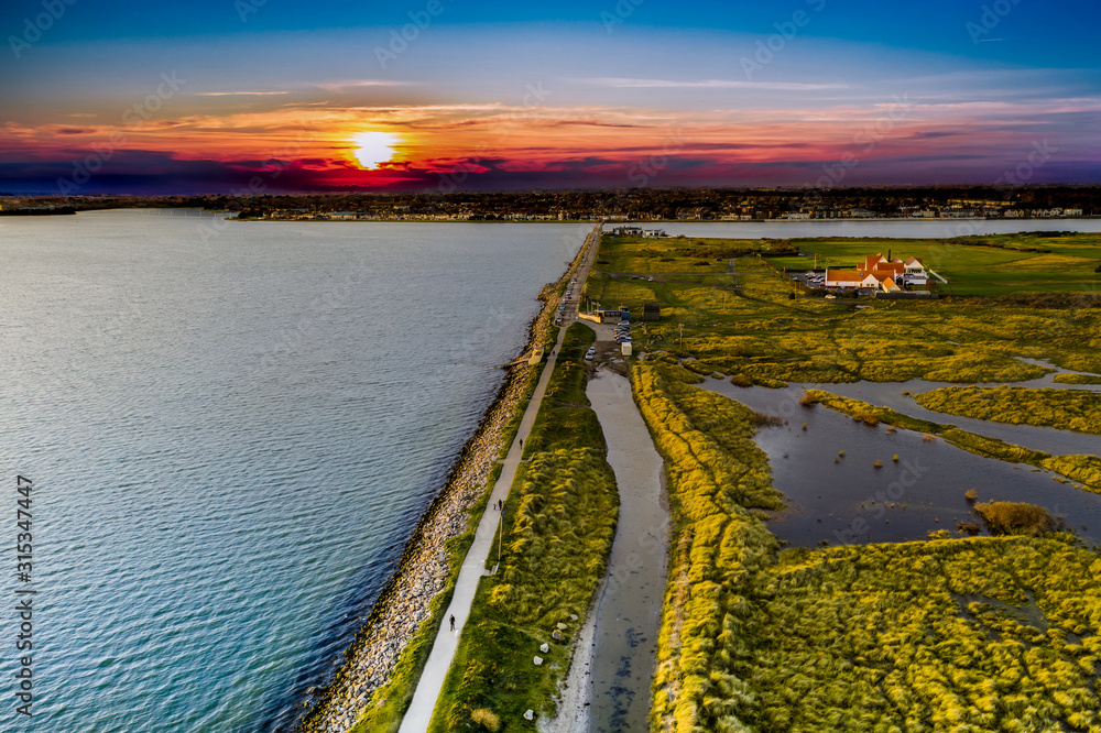 Obraz premium Bull Island aerial view at sunset, revealing marram-grass-anchored dunes and Dublin city on the horizon. North Bull Island, is an island located in Dublin Bay. Autumn view with flooded dunes.