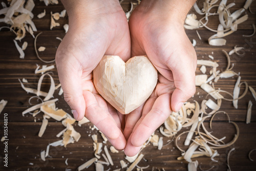 DIY romantic gift. Men's hands hold a wooden heart. Handmade symbol of love for Valentine's Day.
