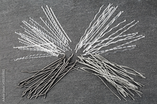 Close up, top down view of a set of four different types concrete reinforcement macro fibers - hooked end steel, white polypropylene sinusoidal and crimped, and grey colored twisted