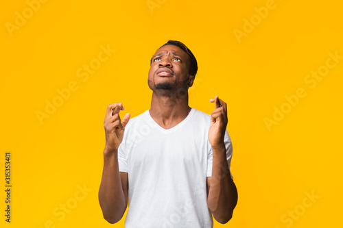 African American Man Keeping Fingers Crossed Standing Over Yellow Background