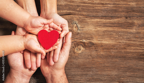 Fototapeta Naklejka Na Ścianę i Meble -  family hands holding red heart on wooden background. Donation, charity, health concept.