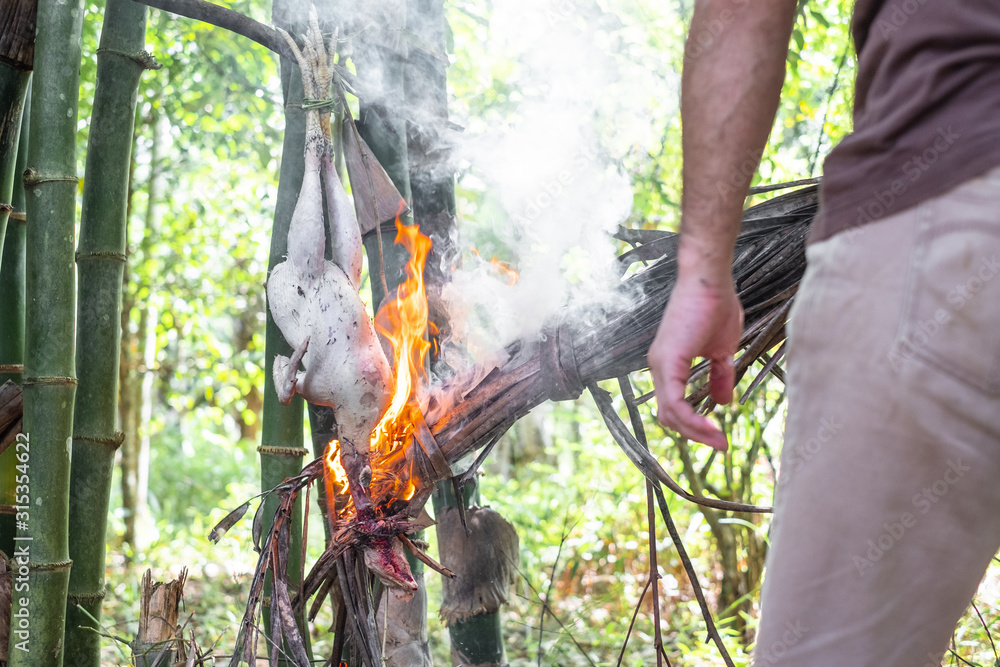Obraz premium Man is roasting chicken with with dry coconut leaves bonfire at camping in the forest.
