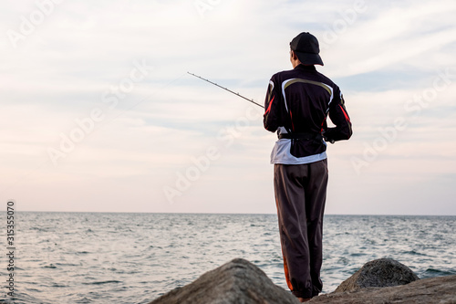 Back view of young man fishing on the beach at the evening time with blue sky background.