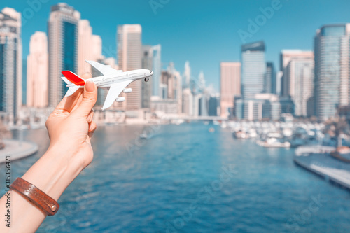 Photography A hand holds a toy white passenger plane against a backdrop of skyscrapers and a seaport