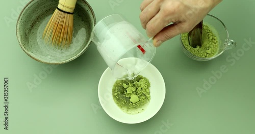 Blending green matcha tea powder in hot water with bamboo whisk to make green matcha tea latte
