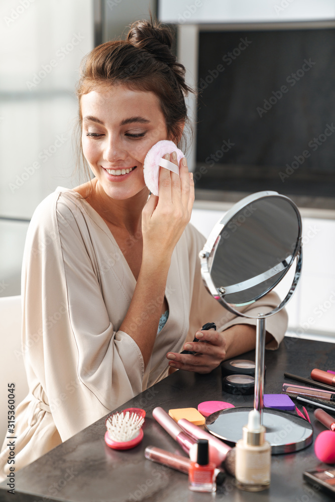 Image of caucasian young beautiful woman applying face makeup at home