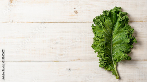 Fotografia Fresh green kale leaf on white wooden tabletop, copy space left