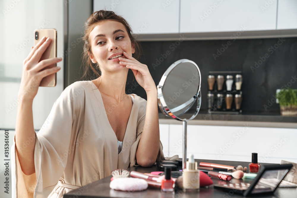 Image of young woman taking selfie photo while applying face makeup Image of young woman taking selfie photo while applying face makeup
