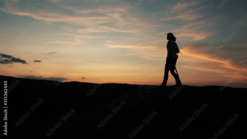 Woman walking with stick on top of a mountain in the golden and blue sunset. Girl silhouette looking at the horizon. Golde hour Woman walking with stick on top of a mountain in the golden and blue sunset. Girl silhouette looking at the horizon. Golde hour