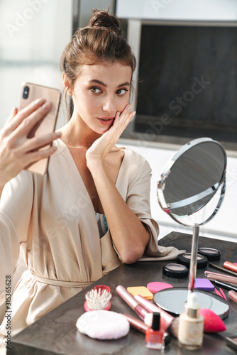 Image of young woman taking selfie photo while applying face makeup