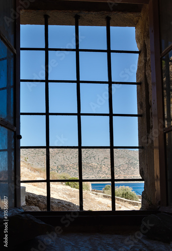 view from an old building through a window with metal bars on the mountains and the sea  Greece