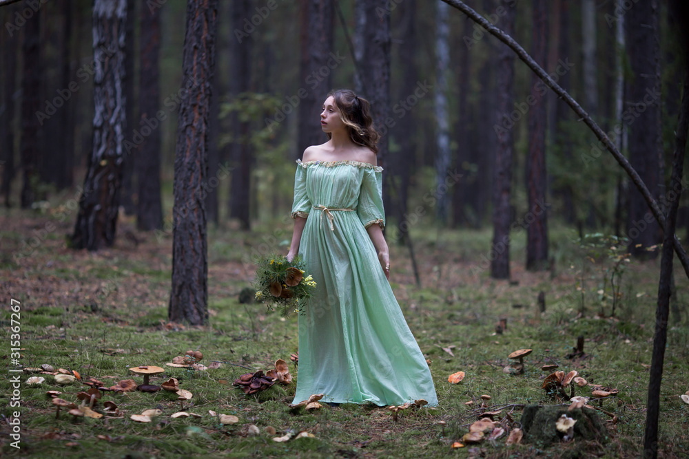 a beautiful girl in a green dress walks in the forest with a bouquet