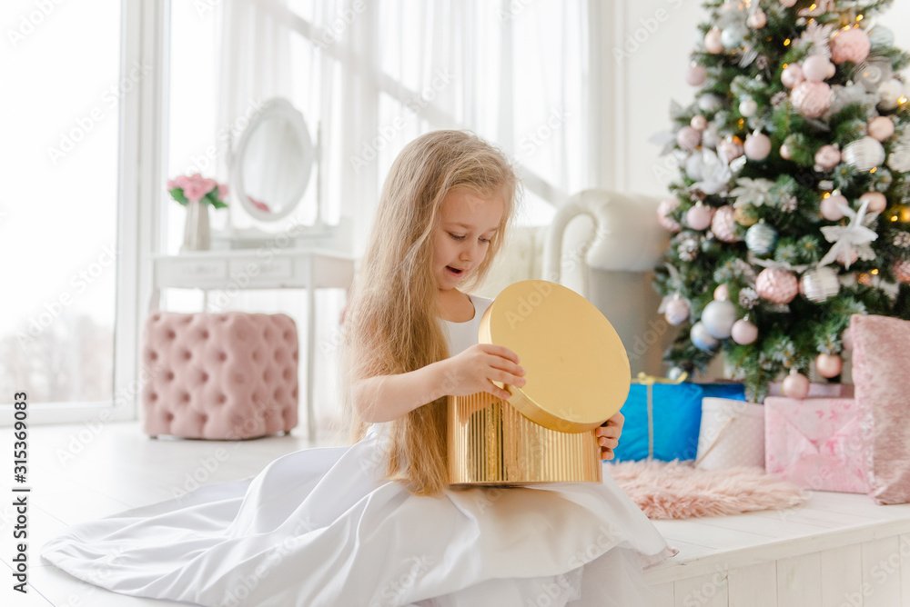 Little blonde girl opens presents at Christmas.