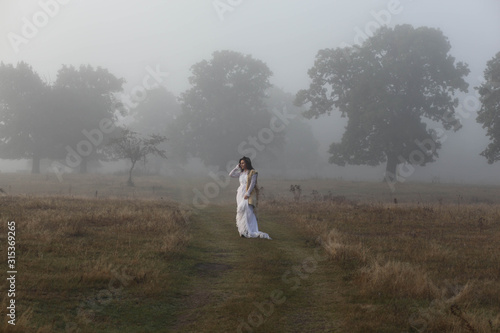 Fototapeta Naklejka Na Ścianę i Meble -  girl in a white dress on a mist field with oaks
