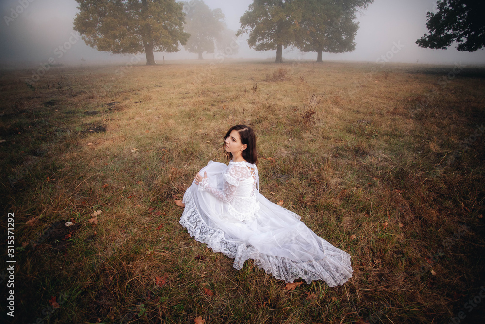 girl in a white dress on a mist field with oaks