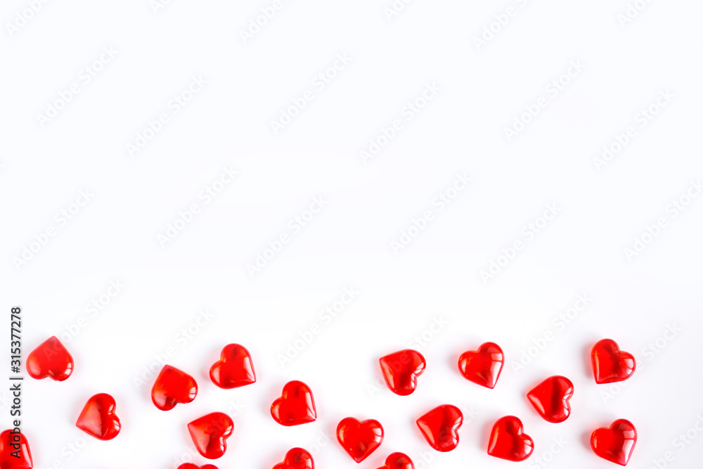 Valentine's Day holiday celebration concept. Red glass hearts laid out in the form of a strip along the bottom edge of the image on a white background. Layout with place for your text.