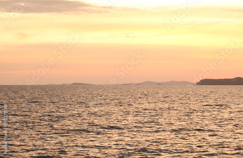 The seaside at sunset has dark shadows in the form of mountains.