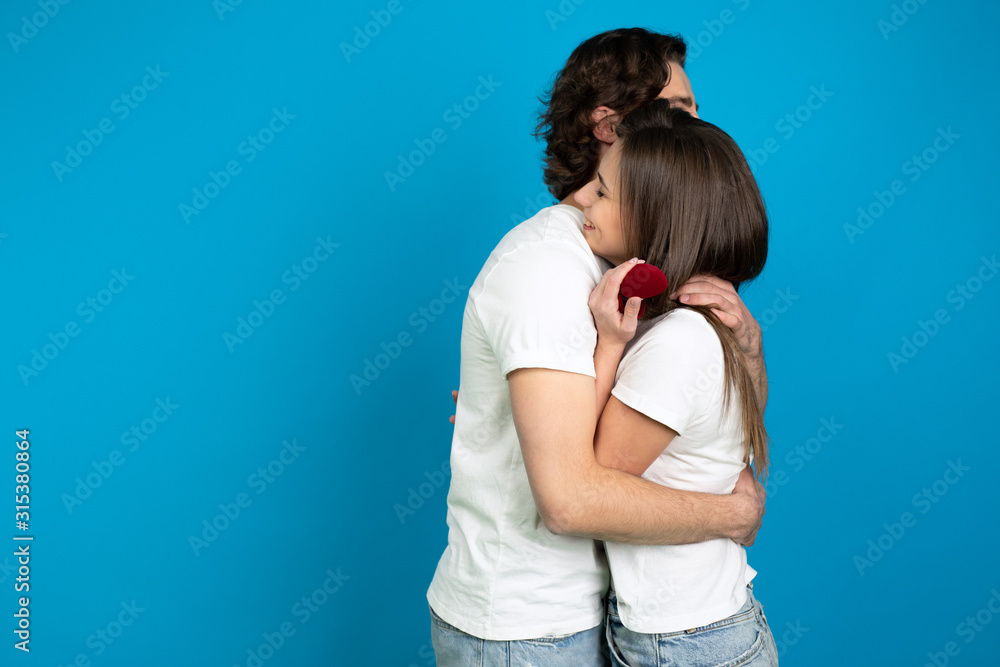 Fototapeta premium Smiling couple with proposal ring embracing isolated on blue background