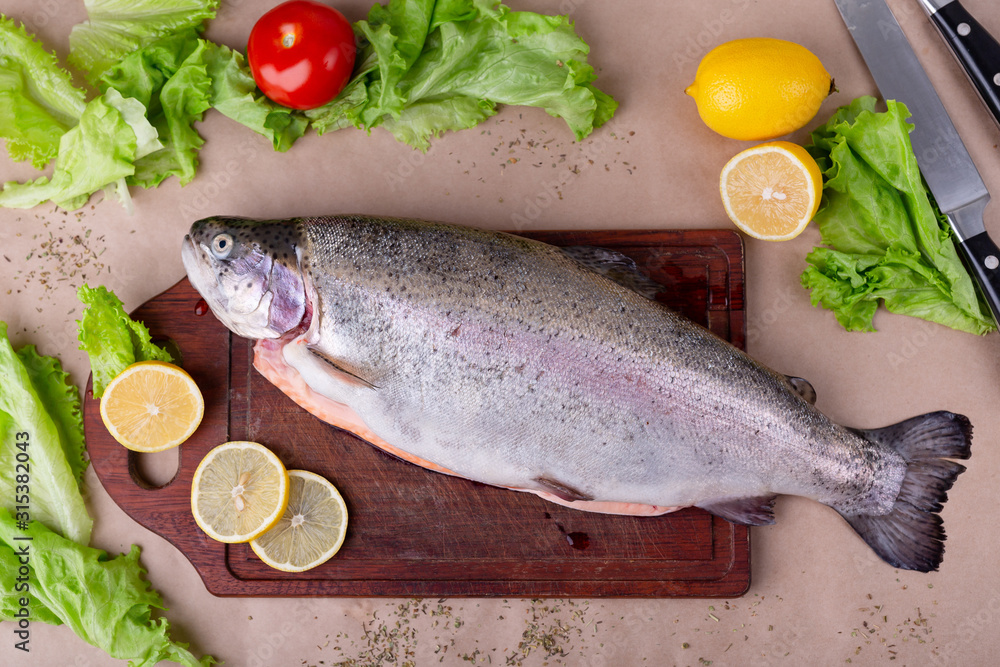Raw fresh unprepared salmon fish on a wooden board with ingredients for cooking. Lemon, lettuce, tomatoes. Mediterranean cuisine, top view, flat lay. Raw fresh unprepared salmon fish on a wooden board with ingredients for cooking. Lemon, lettuce, tomatoes. Mediterranean cuisine, top view, flat lay.