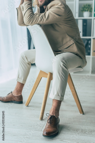 cropped view of elegant fashionable businessman posing on chair in office