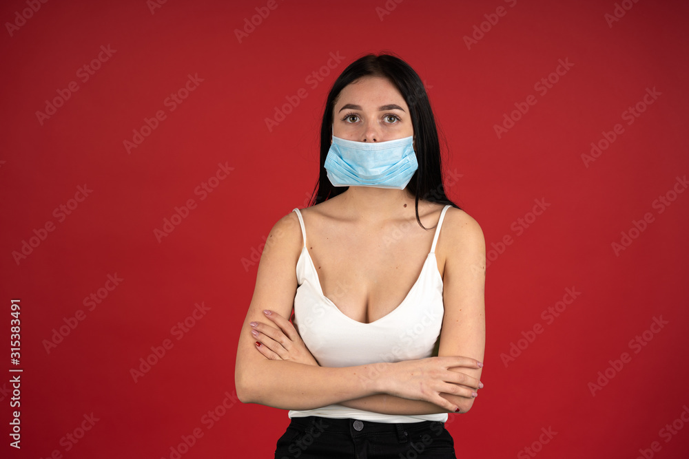 Front view of sick woman in medical mask standing with folded arms isolated on red background Front view of sick woman in medical mask standing with folded arms isolated on red background
