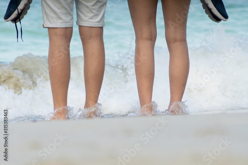 Sweetheart couple legs standing against wave over beach and white sand