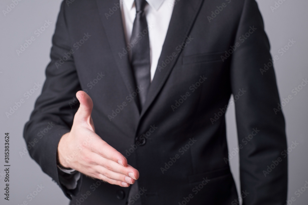 Portrait of a man in a business suit holding out his hand for a handshake. Minimalistic business concept. On a gray background.