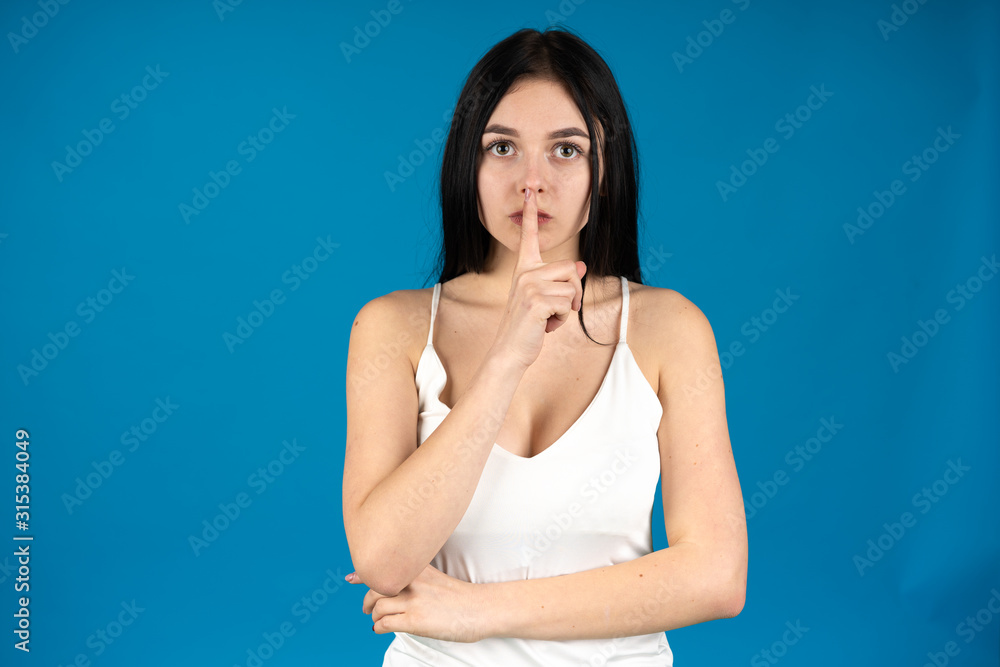 Front view of brunette girl showing silence gesture isolated on blue background Front view of brunette girl showing silence gesture isolated on blue background