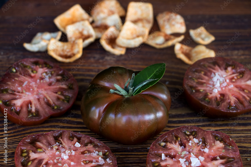 Fototapeta premium Schwarze tomate mit tomatenscheiben und chips aus humus mit tomate