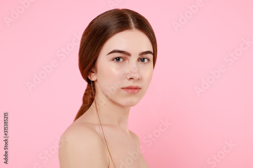 Beautiful young girl touching her perfect skin on pink background.