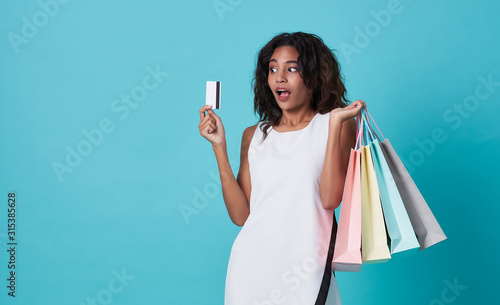 Excited young woman showing credit card and shopping bags isolated over blue background.