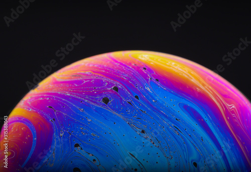 Close up macro photograph of the psychedelic rainbow of colors mixing and swirling in a soap bubble to look like a fantasy galaxy or planet isolated against a black background photo