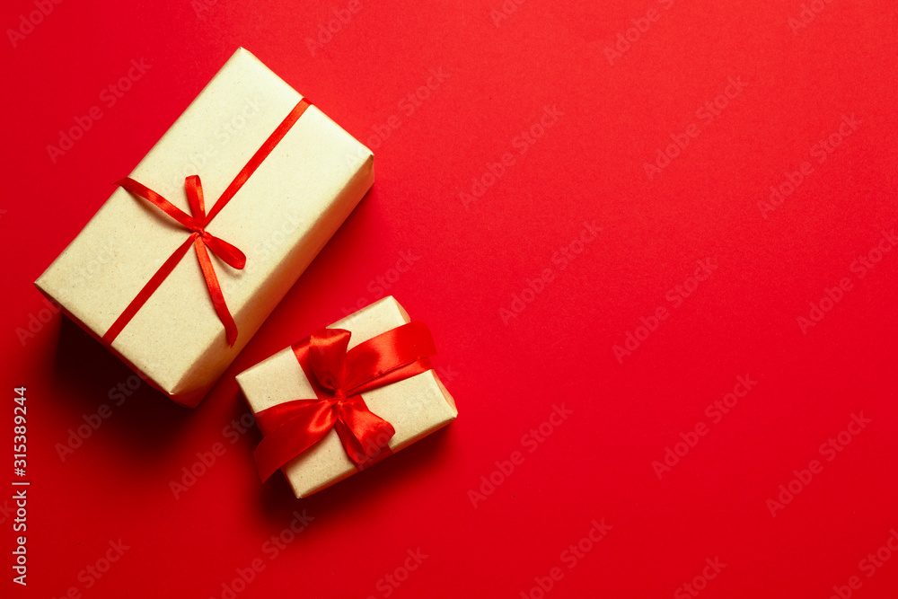 Top view of red minimalistic background with surprise gifts in brown paper and red silk ribbon with copyspace Top view of red minimalistic background with surprise gifts in brown paper and red silk ribbon with copyspace
