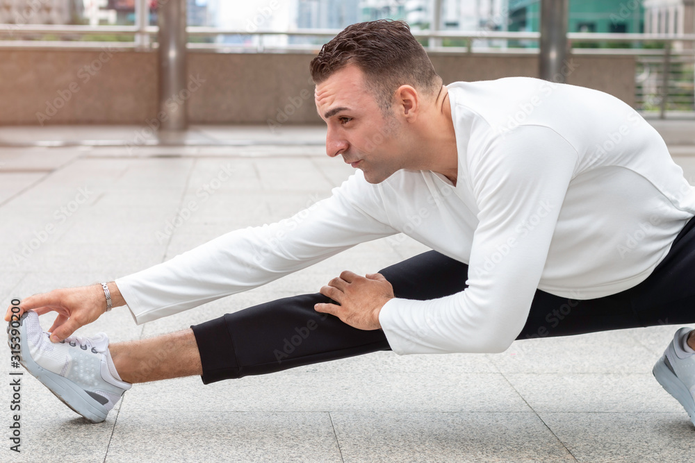 Athletic Caucasian man stretching body, doing exercises on street.
