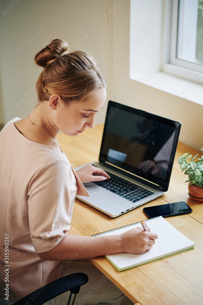 Vertical High Angle shot of young woman sitting at table working on something iin modern office Vertical High Angle shot of young woman sitting at table working on something iin modern office