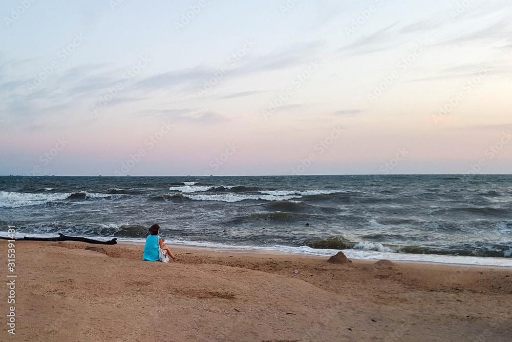 Girl sitting on the beach in a storm and looking at the sea Girl sitting on the beach in a storm and looking at the sea