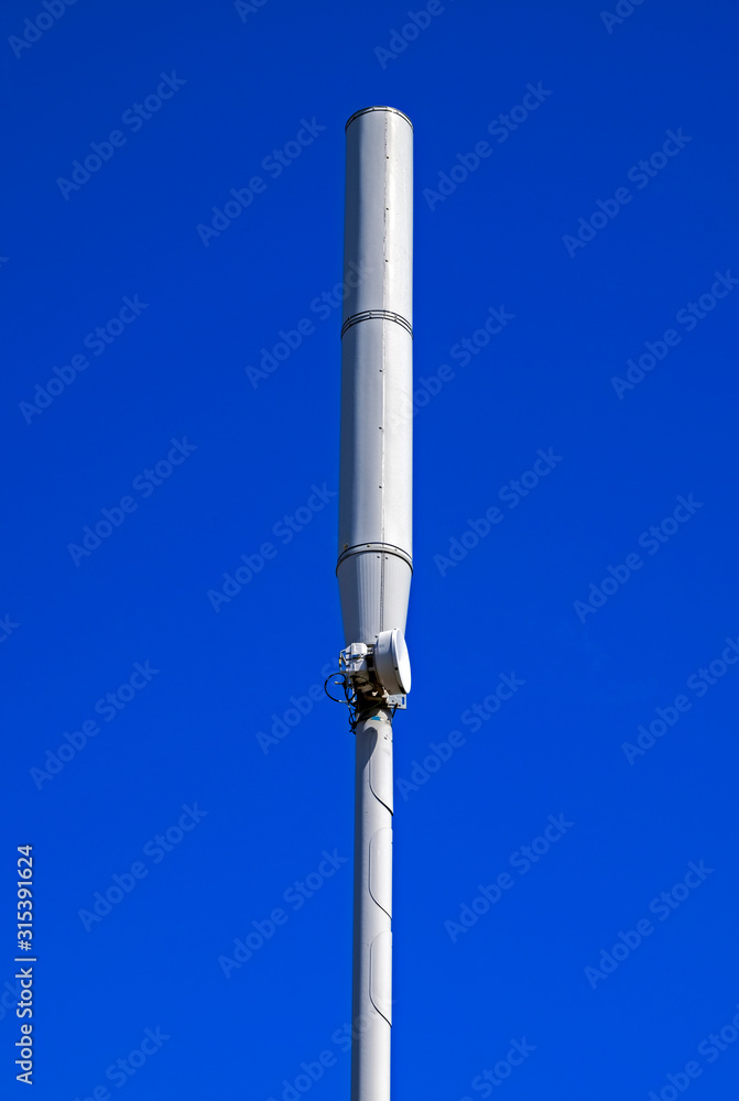 A mobile phone mast in a town in the UK seen against a clear blue sky A mobile phone mast in a town in the UK seen against a clear blue sky